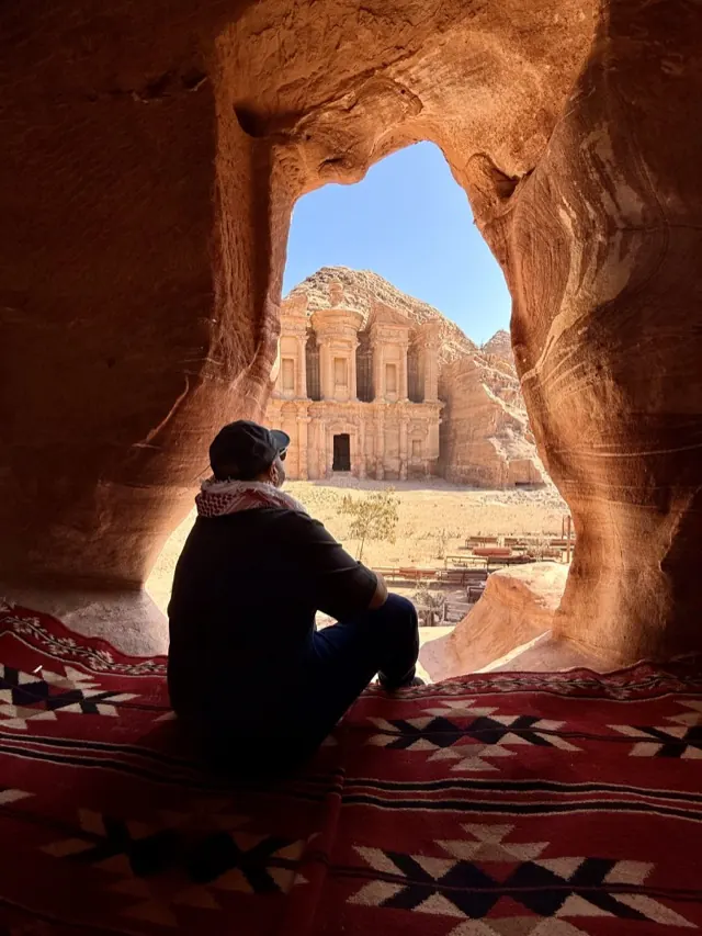 Hassan seated in a rock alcove looking out at the Monastery carved into the cliffs of Petra in Jordan